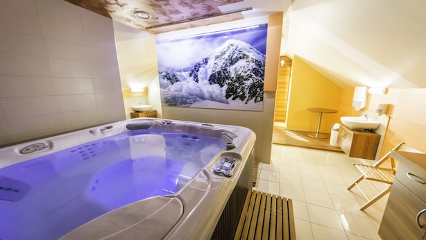 A modern spa room with a hot tub, wooden flooring, a wall-mounted sink, and a large framed picture of a snowy mountain. - Guesthouse Vodnik (Cerklje na Gorenjskem)