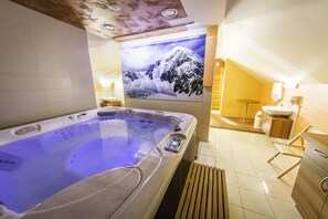 A modern spa room with a hot tub, wooden flooring, a wall-mounted sink, and a large framed picture of a snowy mountain. - Guesthouse Vodnik (Cerklje na Gorenjskem)