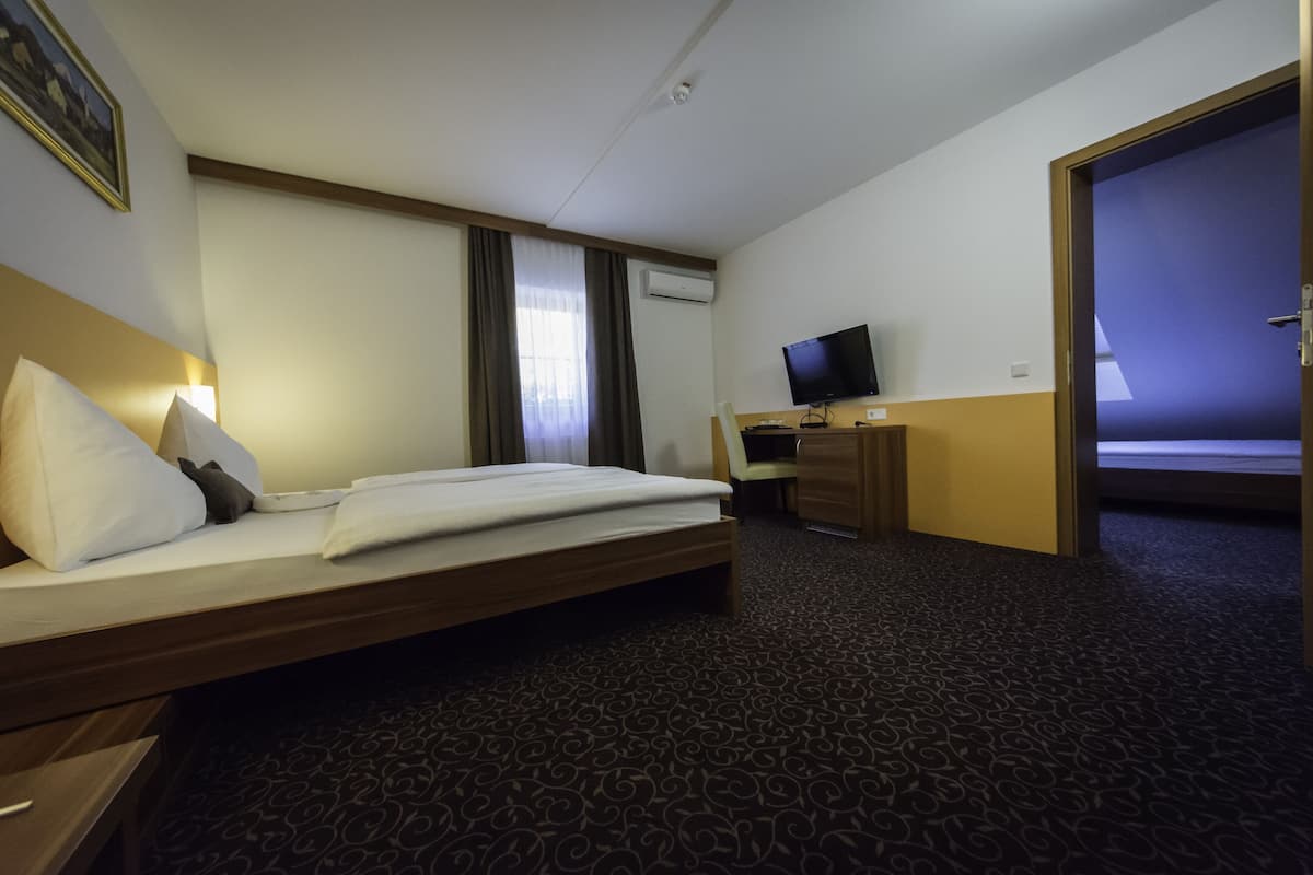 Una habitación de hotel con cama, escritorio con computadora, televisión y aire acondicionado.
