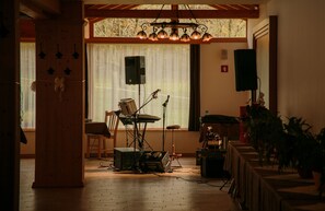 A room with a wooden floor, a drum set, a keyboard, and a microphone stand. There is a window with curtains and a chandelier. - Guesthouse Vodnik (Cerklje na Gorenjskem)