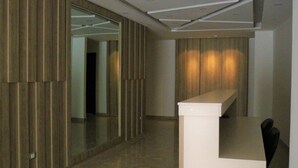 A modern interior with a reception desk, wooden panel walls, and a glass door leading to another room. - Amazing one Bedroom Apartment in Amman, Elwebdah 7 (Amman)