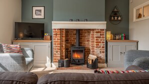 Ein gemütliches Wohnzimmer mit Kamin aus Ziegelsteinen, grauen Sofas, einem Fernseher und einem Bücherregal.