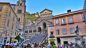 Una plaza animada con edificios históricos, una iglesia destacada con un campanario y una estatua en primer plano.