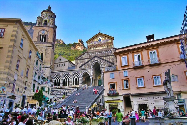 Una plaza animada con edificios históricos, una iglesia destacada con un campanario y una estatua en primer plano.