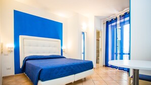 Una habitación de hotel con una cama grande, un cabecero blanco, cortinas azules y una mesita.
