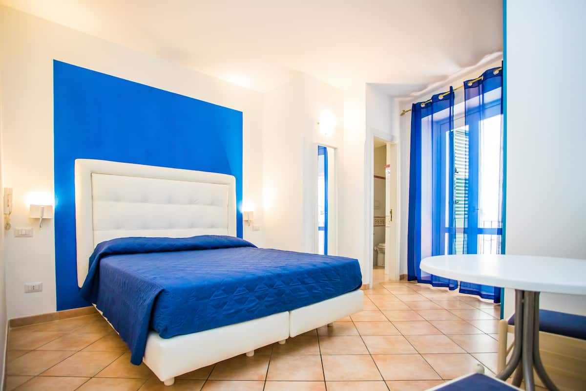 Ein Hotelzimmer mit einem großen Bett, einem weißen Kopfteil, blauen Vorhängen und einem kleinen Tisch.