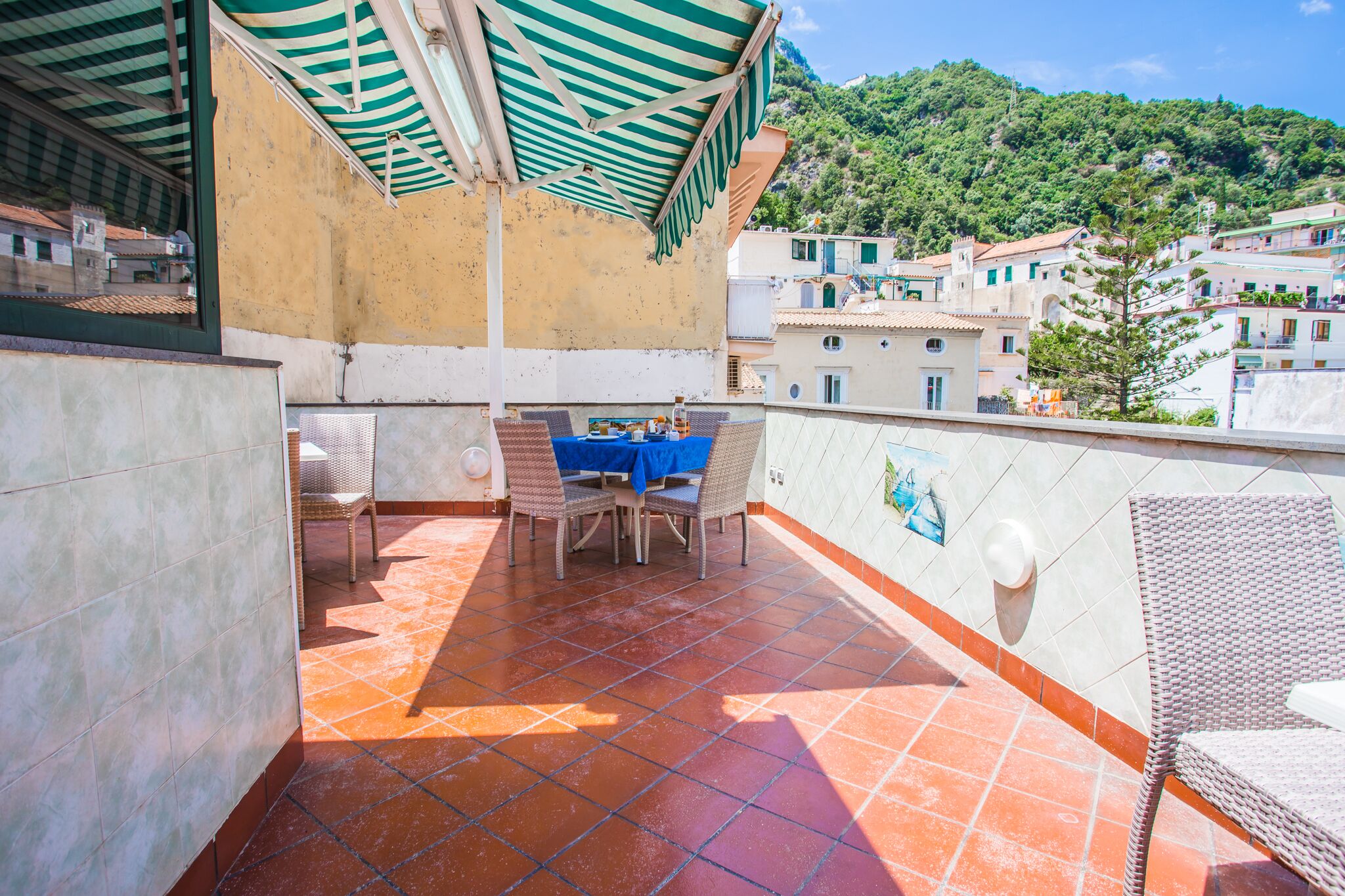 A terrace with a table and chairs, a tiled floor, and a view of a hillside town.