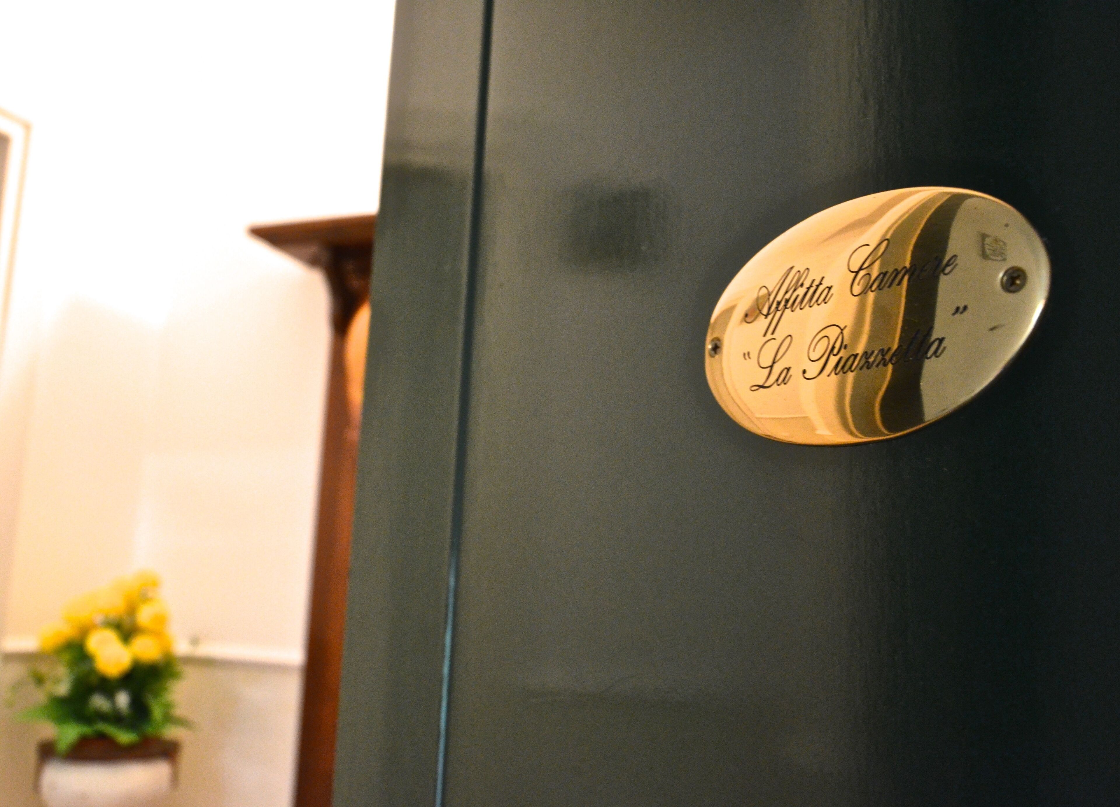 A metallic plaque with the inscription "Affitta Camera La Passerella" on a dark-colored door.