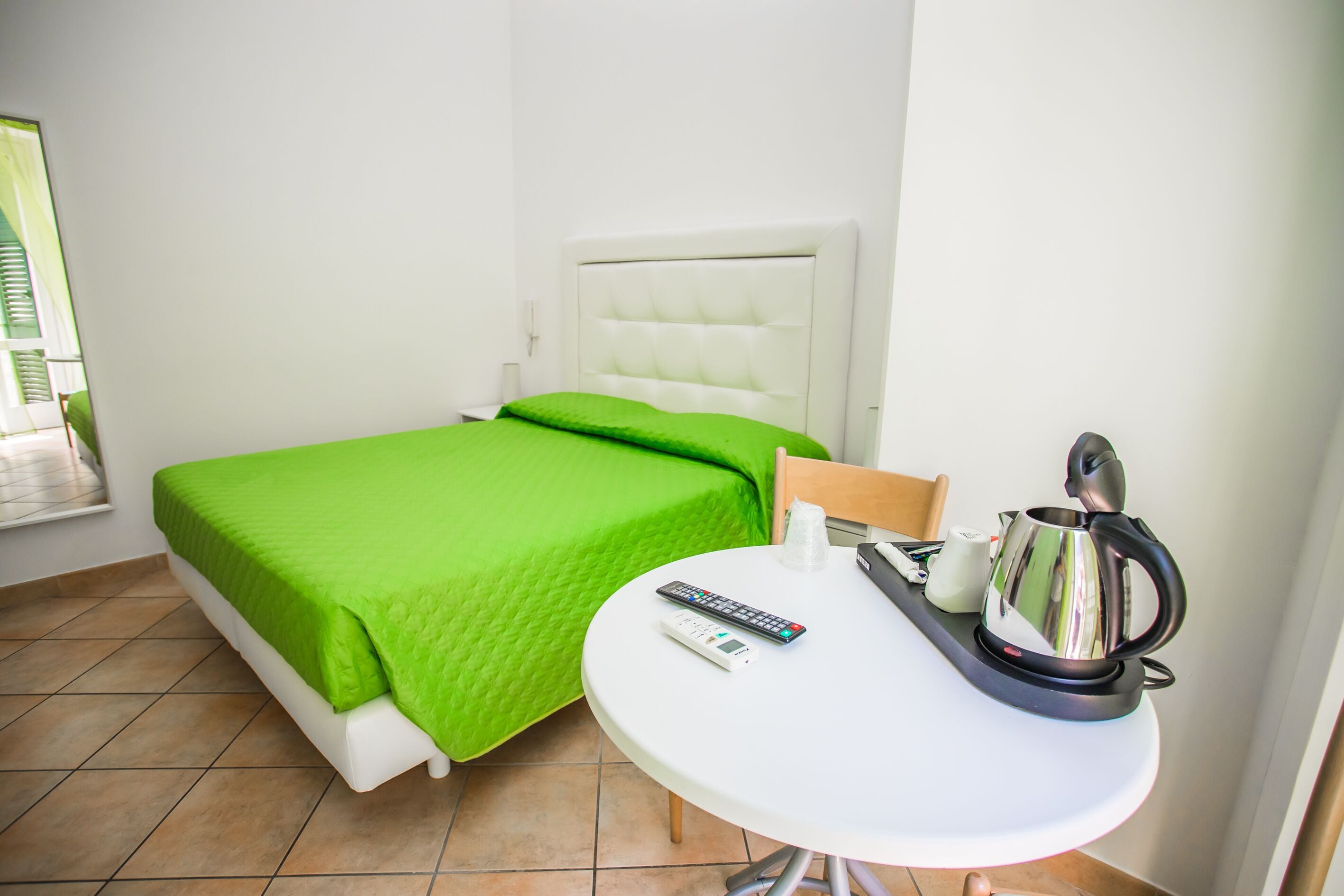 Une chambre d’hôtel avec un lit, une petite table avec une bouilloire, une télécommande et une prise de courant.