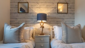 Ein Doppelbett mit einer weißen und blauen Decke, ein Nachttisch mit Lampe sowie eine Holzwand mit zwei Spiegeln.