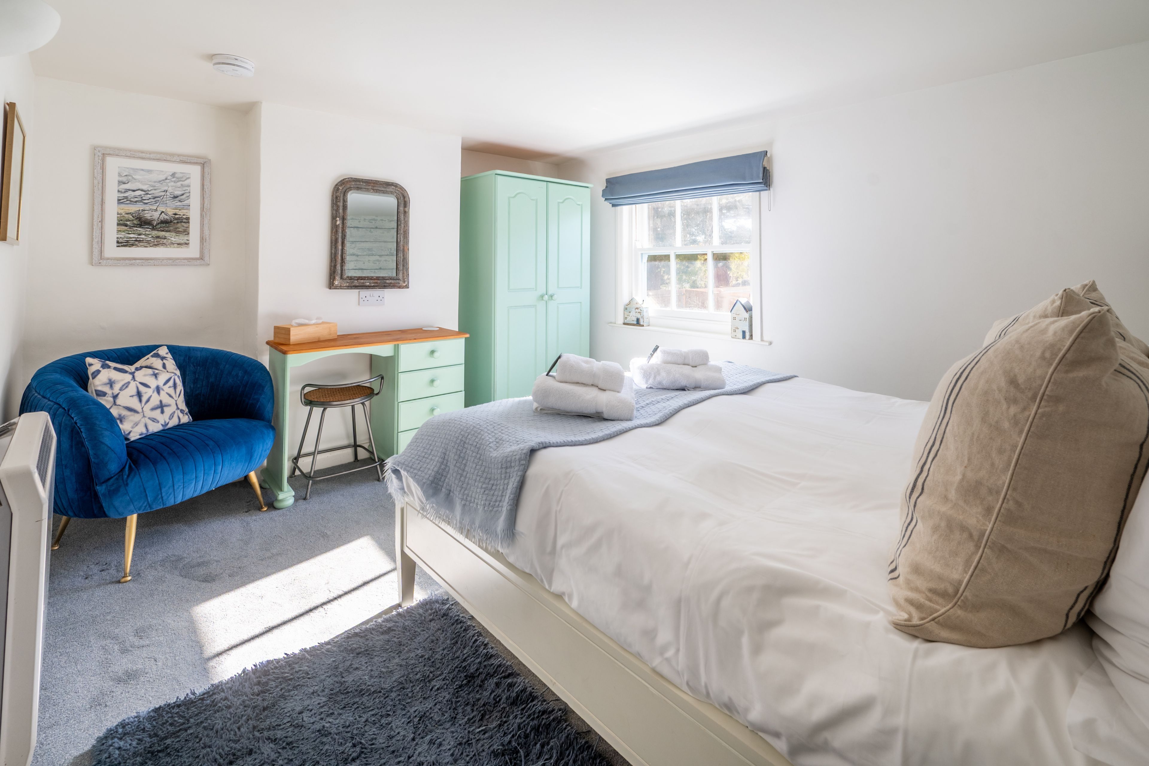 Un dormitorio con cama, una silla, un escritorio, un armario y una ventana.