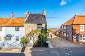 A traditional stone building with a slate roof, a white building with a blue door, and a gravel driveway. - Bracken Cottage, Brancaster Staithe, Norfolk (Brancaster Staithe)