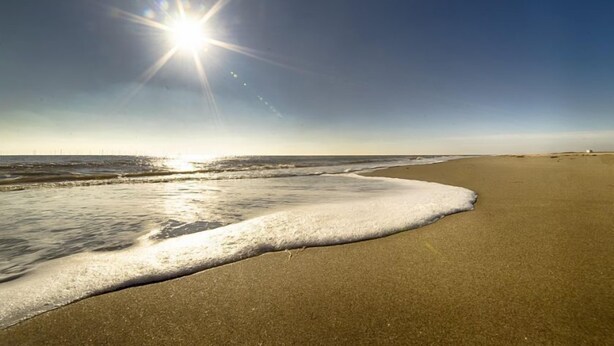 Ein Strand mit blauem Himmel und Sonnenlicht, das sich im Wasser spiegelt.