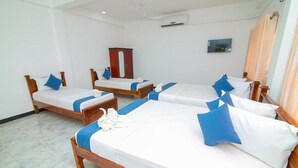 Habitació d'hotel amb quatre llits de fusta, cadascun amb roba de llit blanca i naxes blaves. Hi ha un armari de fusta i un televisor de pantalla plana penjat a la paret.