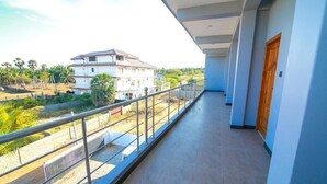 A balcony with a metal railing, a view of a building, and a paved area with plants. - Sun Blue Guest House Hotel (Alas Garden Trincomale Trincomale)