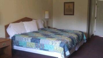 Quarto com cama, mesa de cabeceira, abajur e porta.