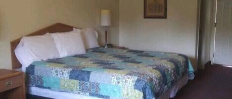A bedroom with a bed, a nightstand, a lamp, and a door.