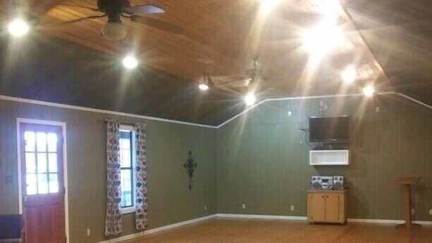A spacious room with wooden floors, a ceiling fan, a television, and a cabinet. - Whispering Creek Lodging & RV Resort (Newton)