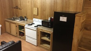 A compact kitchen with wooden cabinets, a white stove, a black microwave, and a black refrigerator. - Whispering Creek Lodging & RV Resort (Newton)