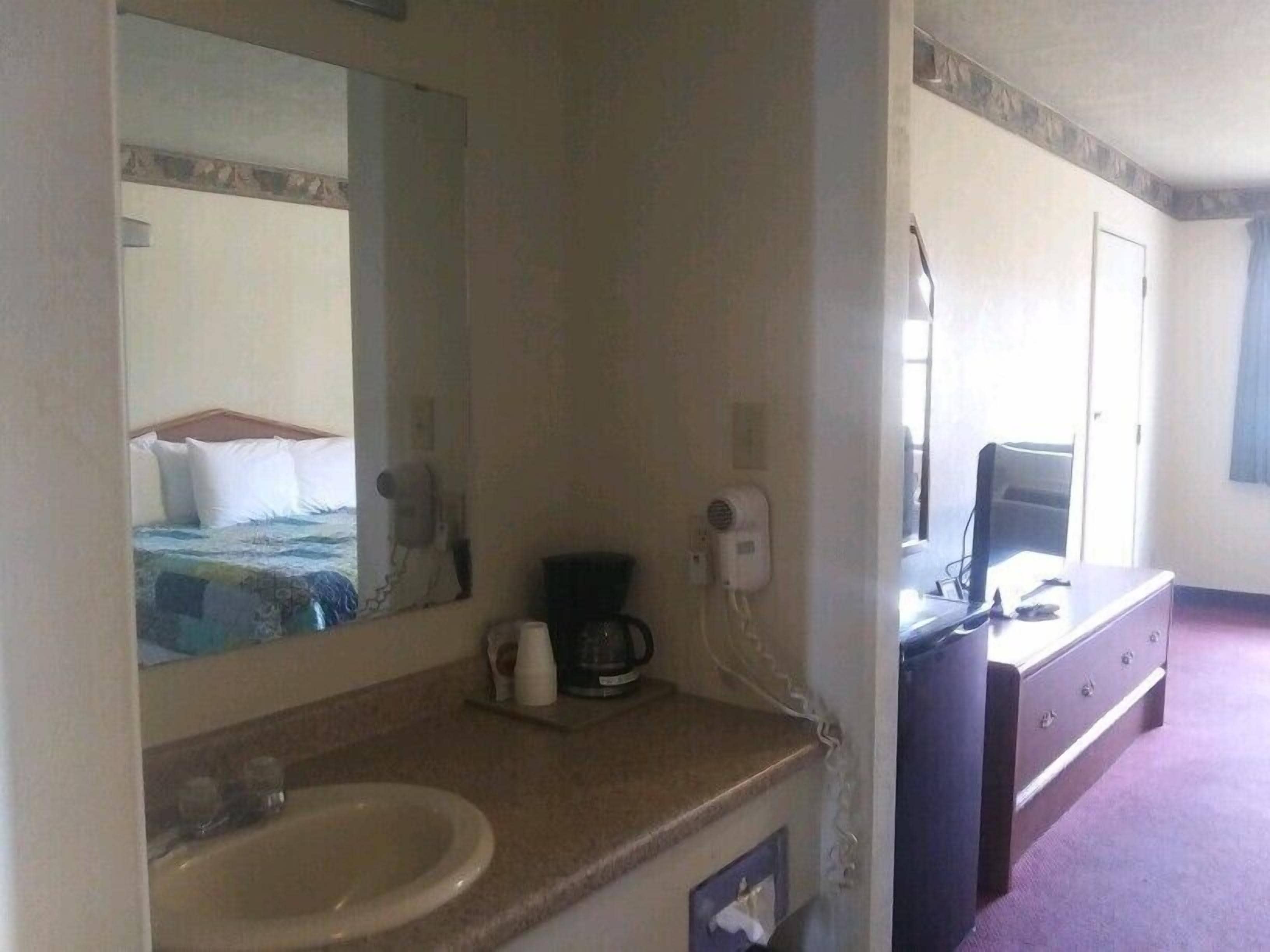 A hotel room with a bed, a large mirror, a sink, a coffee maker, a desk, and a dresser.