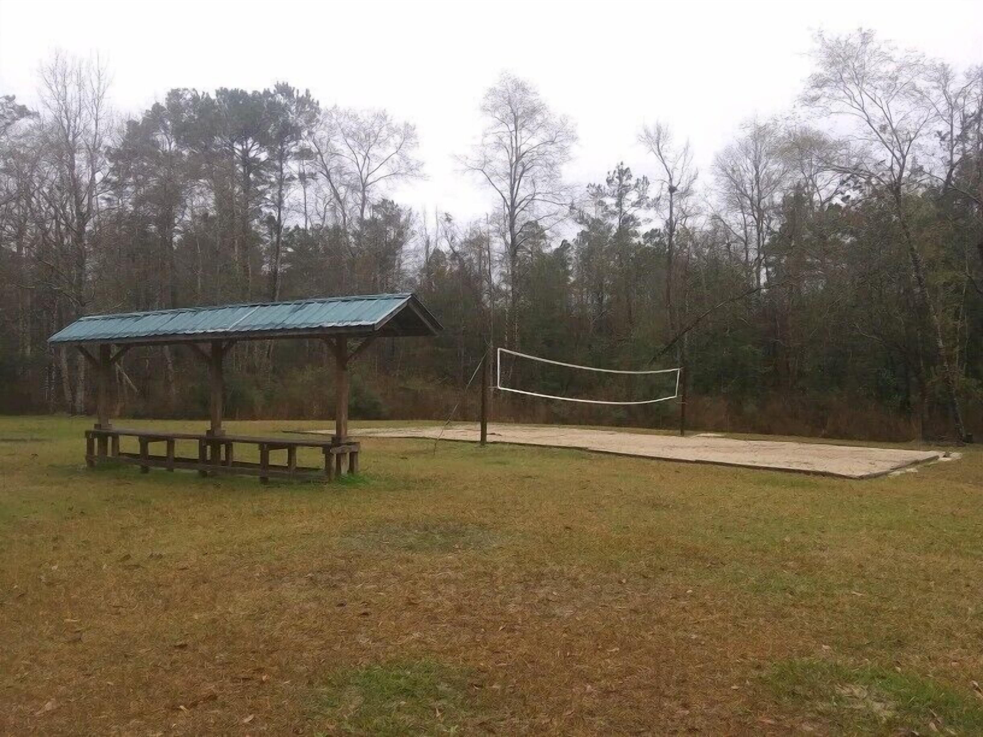 A park with a wooden pavilion and a volleyball net.