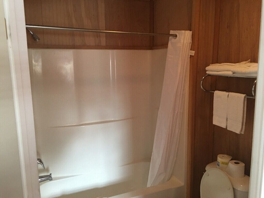 Un baño con bañera, cortina de ducha, toallero con toallas y papel higiénico.