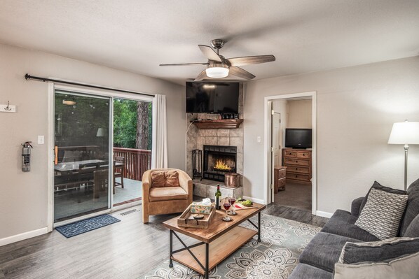 A living room with a fireplace, a ceiling fan, a television, and a sofa. - Midtown Modern Mountain Getaway (Ruidoso)