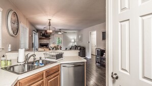A kitchen with a dishwasher, sink, wooden cabinets, and a clock on the wall.