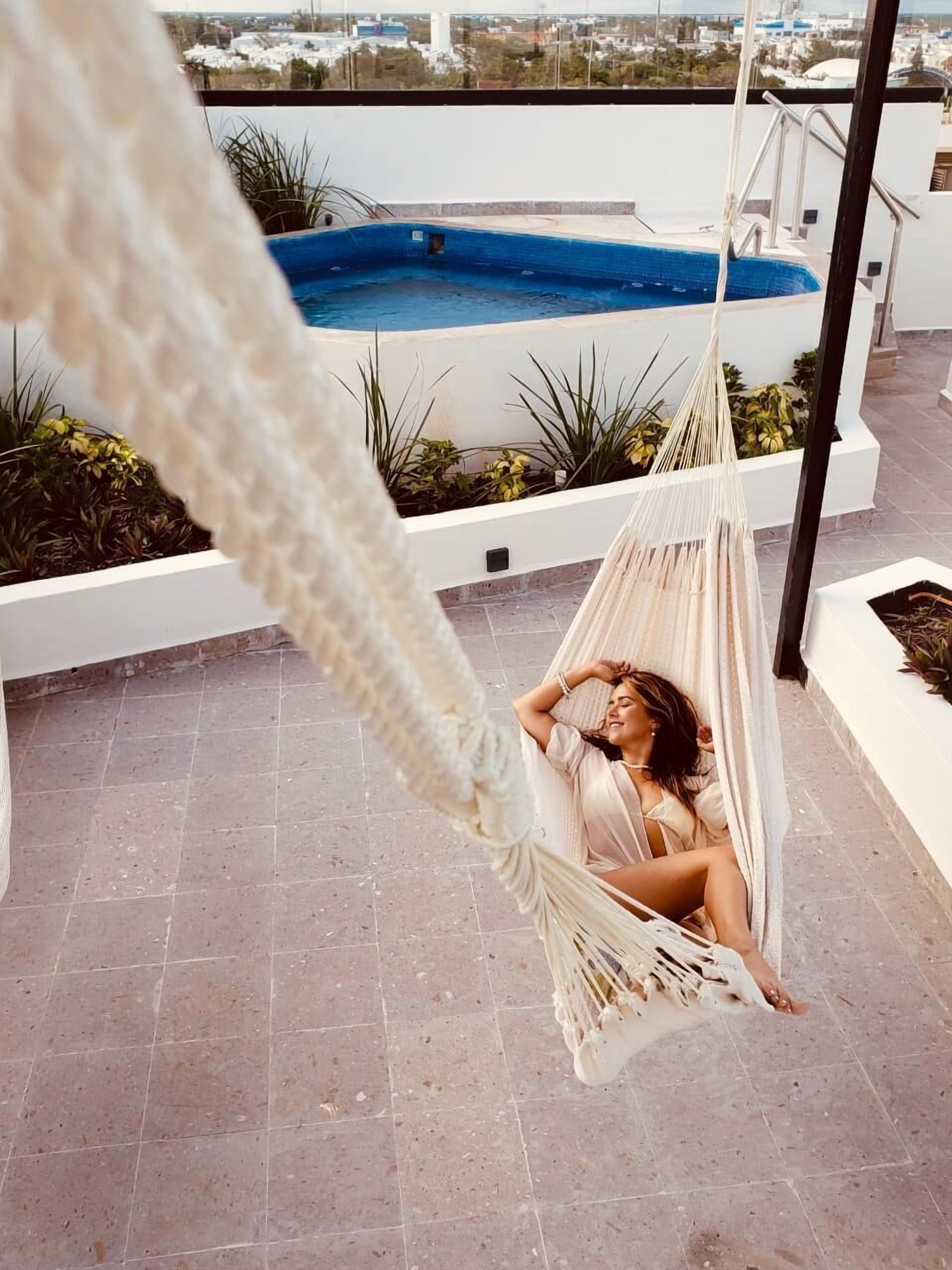 A hammock on a rooftop terrace with a pool and plants in the background.
