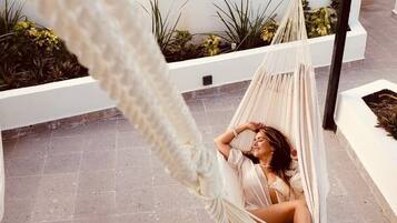 A hammock on a rooftop terrace with a pool and plants in the background.