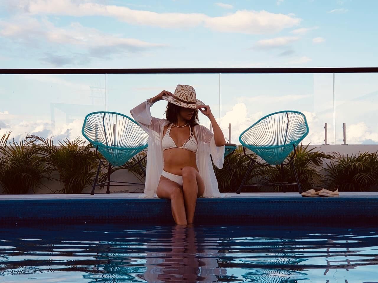 Eine Person sitzt am Pool, im Hintergrund ein klarer Himmel und Palmen.
