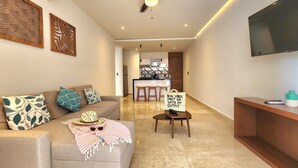 Una sala de estar moderna con sofá, mesa de centro, televisor y cocina al fondo.