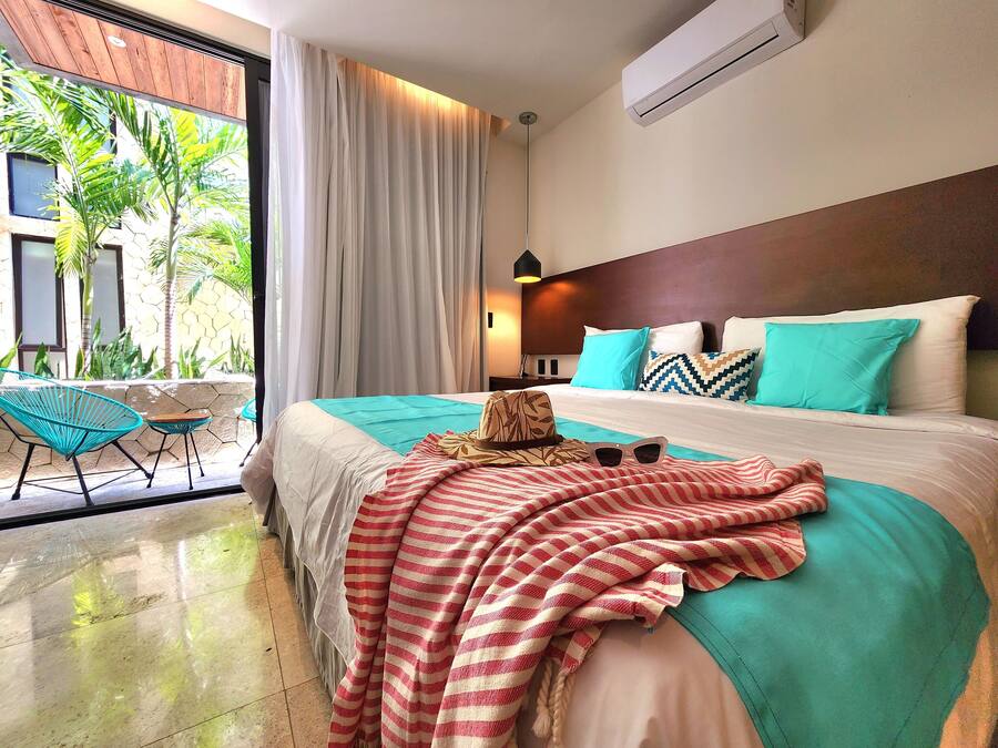 Habitación de hotel con una cama, vista a palmeras y un balcón con sillas.