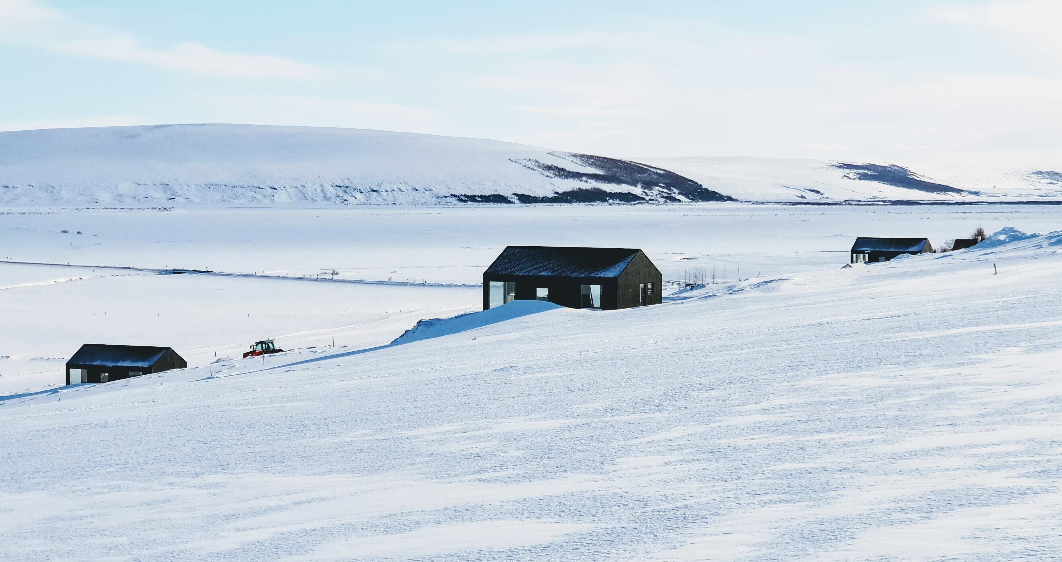 A snow-covered landscape with several small buildings, likely cabins or houses, situated on a slope.