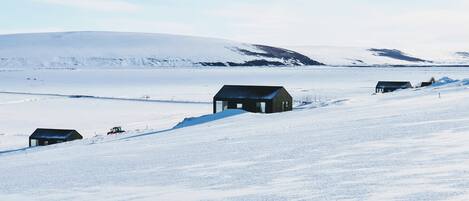 A snow-covered landscape with several small buildings, likely cabins or houses, situated on a slope.