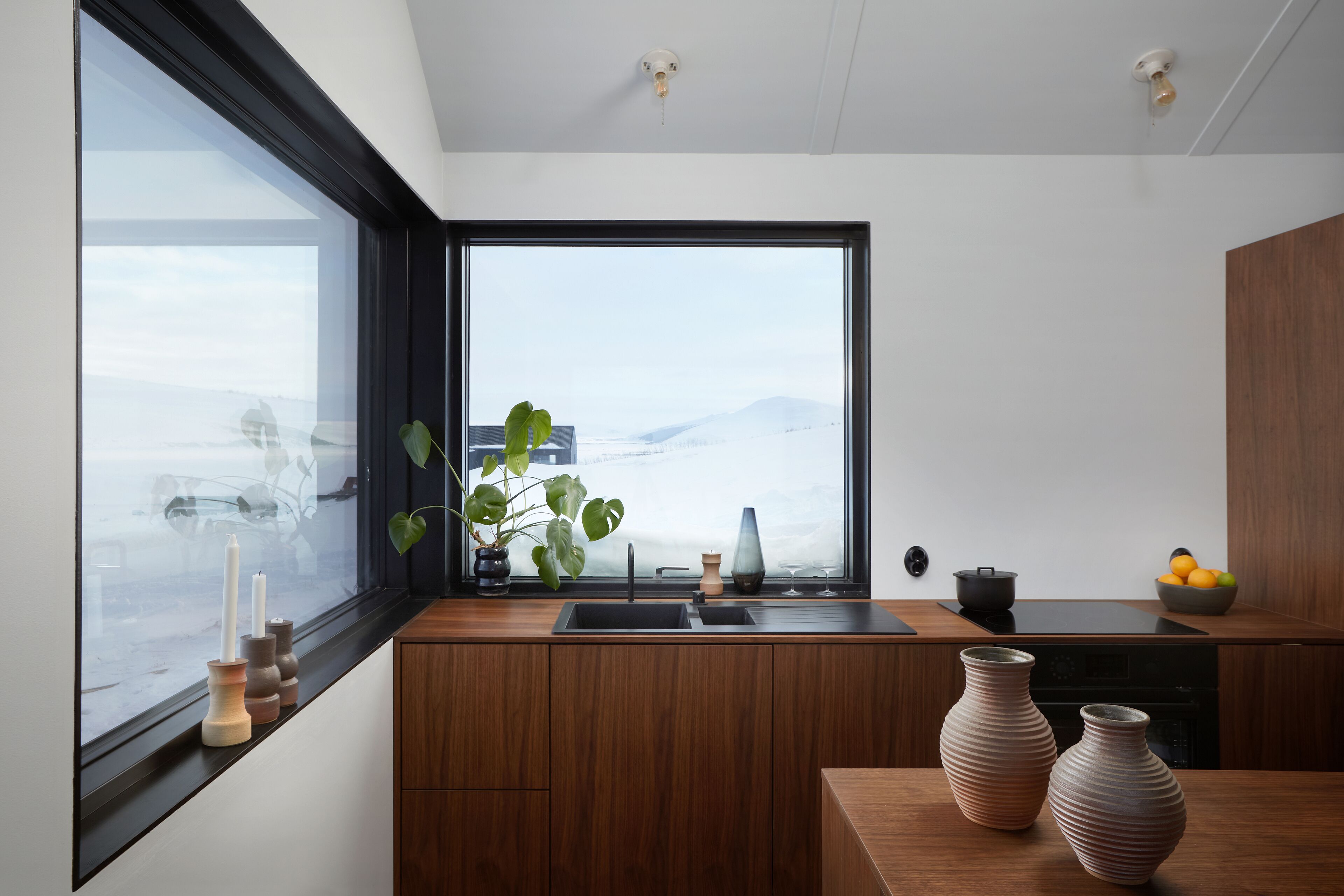 Eine moderne Küche mit einem großen Fenster, Holzschränken, einer Spüle und einer Schüssel mit Obst auf der Arbeitsplatte.