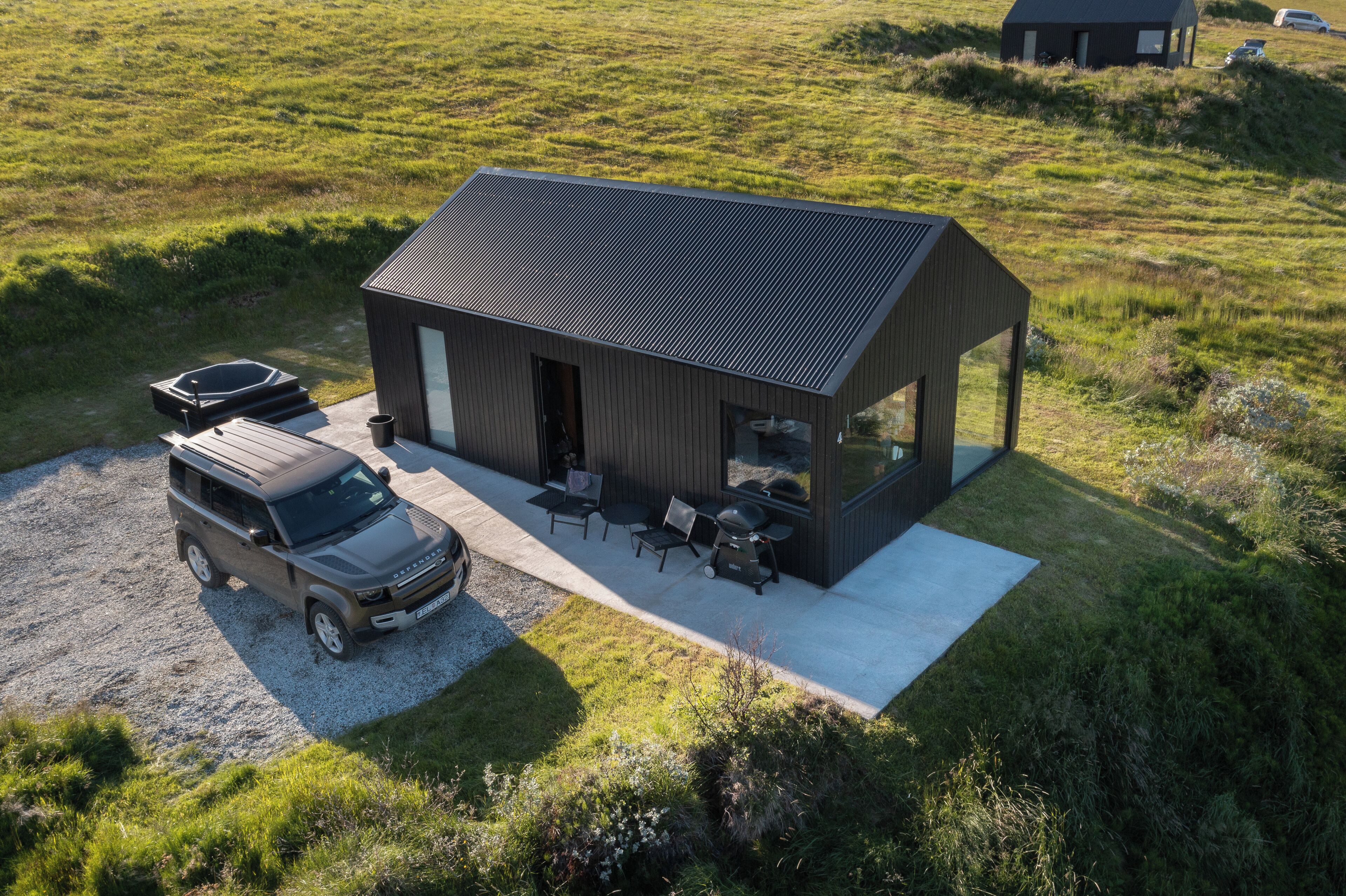 Una casa moderna con entrada de grava, un coche y mobiliario exterior.