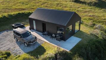 Una casa moderna con entrada de grava, un coche y mobiliario exterior.