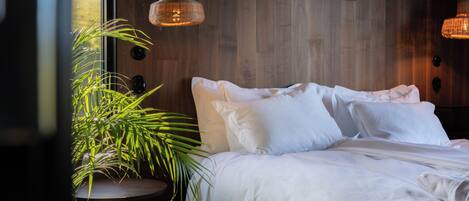 Un dormitorio con pared de madera, una cama con ropa blanca, dos lámparas colgantes y una planta en maceta.