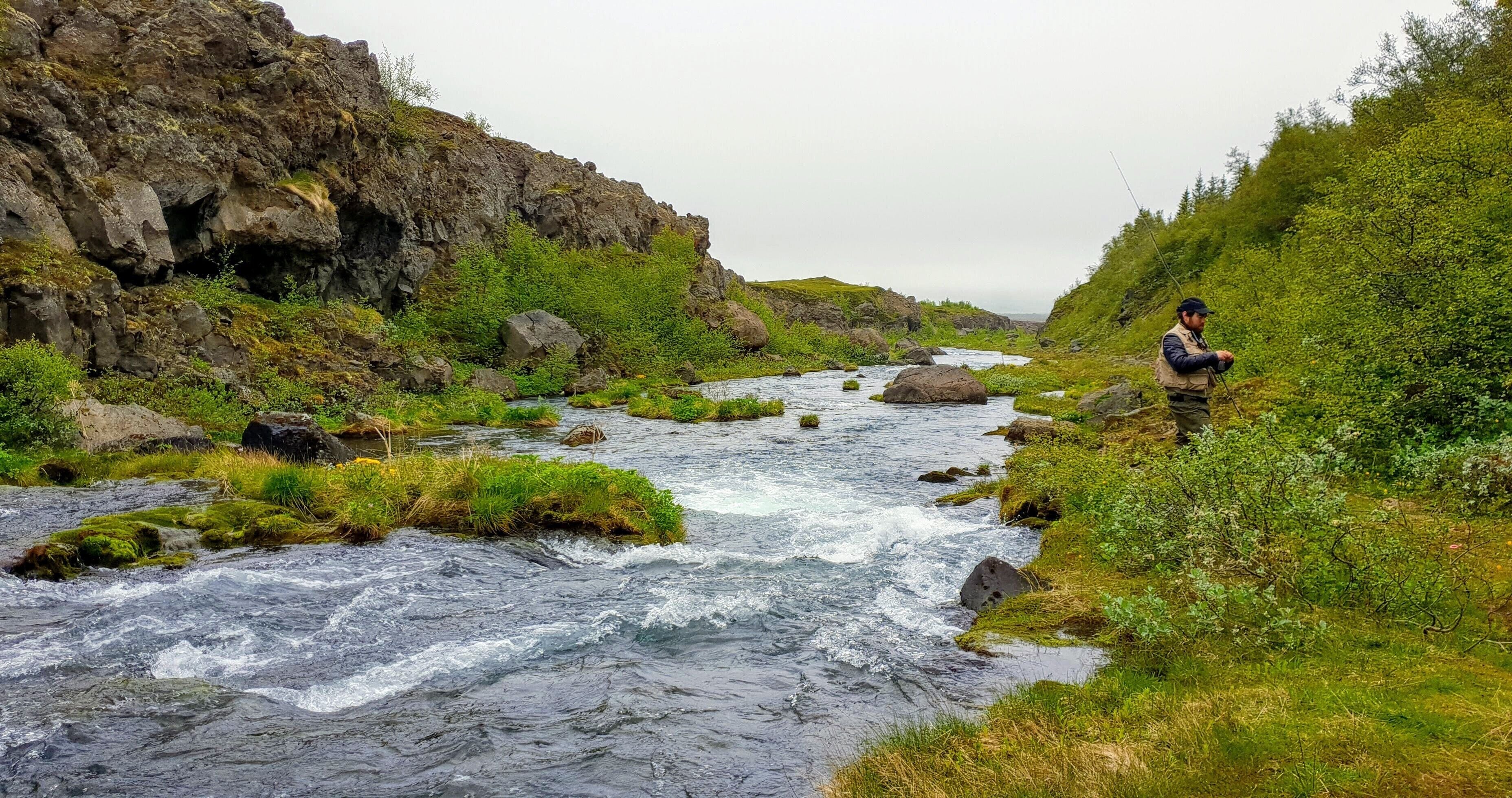 A river flowing through a rocky landscape with a person fishing.