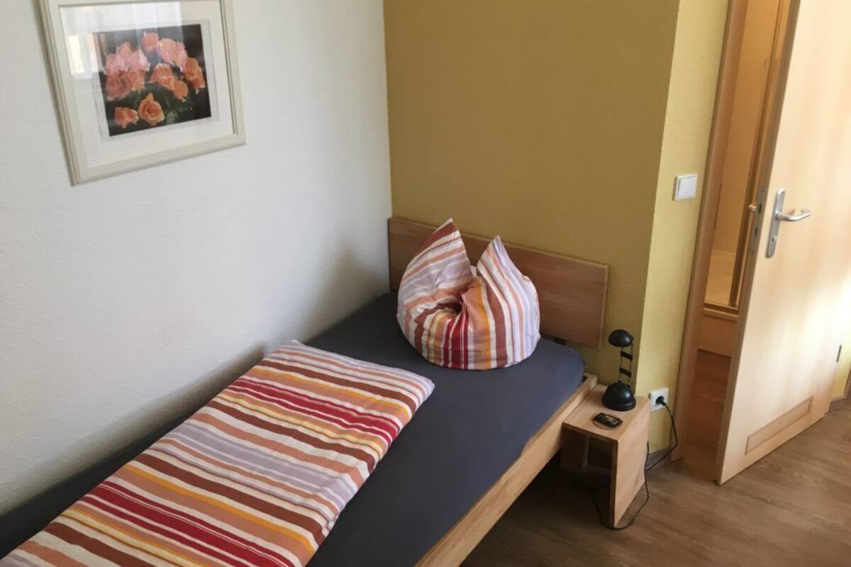 Un lit simple avec une couverture à rayures, un oreiller, une table de chevet avec une lampe et un tableau encadré au mur.