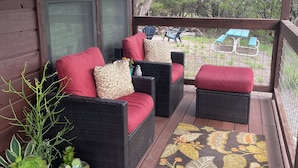Terraza de madera con mobiliario de mimbre y un tapete floral.