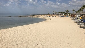 A beach with a sandy shore, palm trees, and beach umbrellas. - Villa 400 Meters Walk To The Beach, Sleep 6, 3 Bedrooms, 5 beds (sotira)