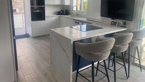 A modern kitchen with white cabinetry, a large island with bar stools, a built-in oven, and a flat-screen TV. - Villa 400 Meters Walk To The Beach, Sleep 6, 3 Bedrooms, 5 beds (sotira)