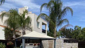 A swimming pool with blue mosaic tiles, surrounded by artificial grass, and a covered patio area with lounge chairs and planters. - Villa 400 Meters Walk To The Beach, Sleep 6, 3 Bedrooms, 5 beds (sotira)