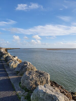 Une promenade en bord de mer, bordée de gros rochers, d’où l’on a une vue dégagée sur la mer.