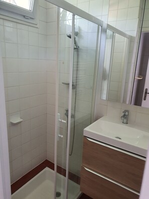 Une salle de bain avec une douche à parois de verre, un lavabo blanc et un meuble en bois.