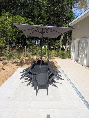 Une terrasse extérieure avec une table et des chaises, un grand parasol et un bâtiment en arrière-plan.