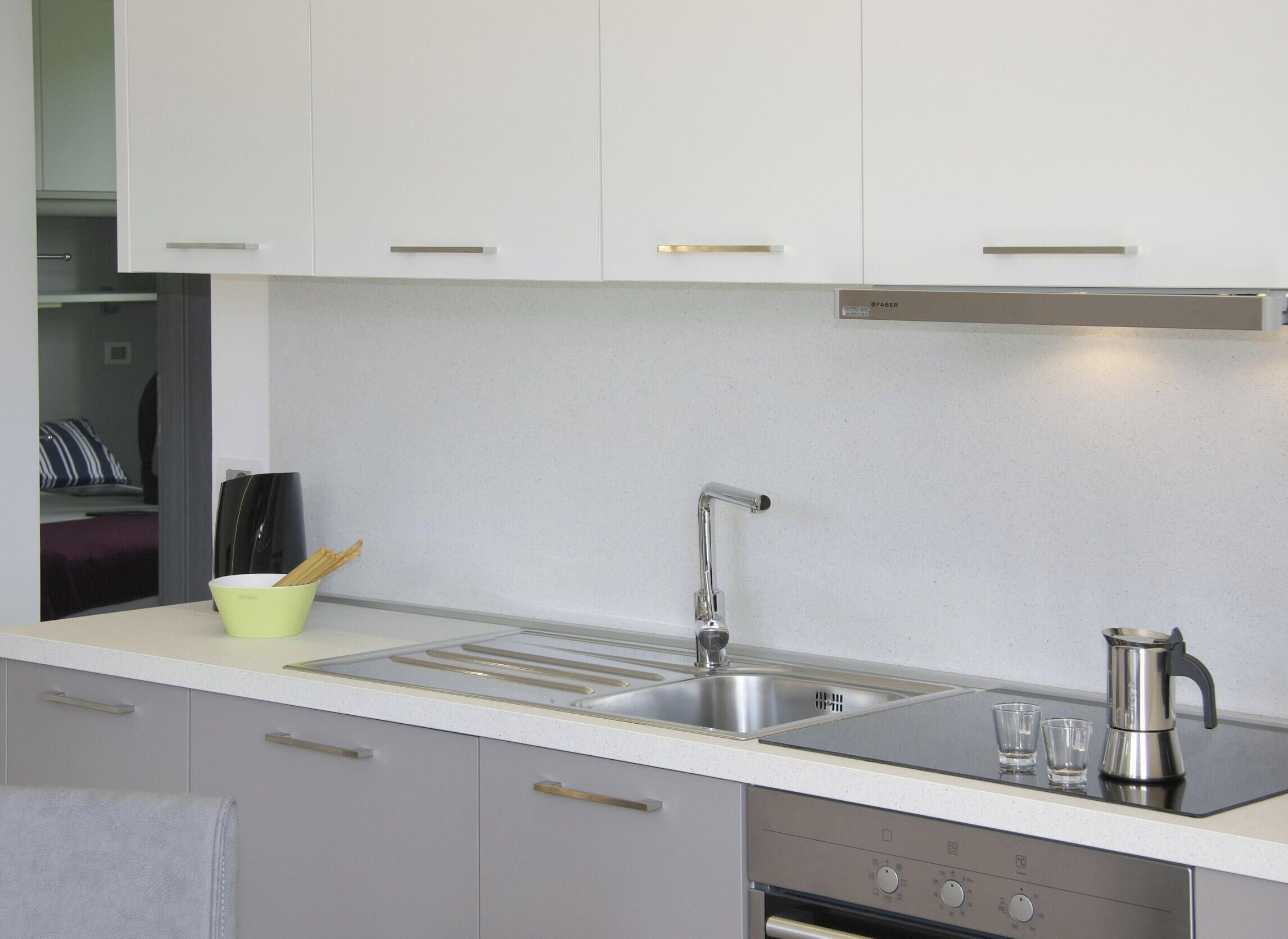 A modern kitchen with a stainless steel sink, a kettle, and a bowl on the countertop.