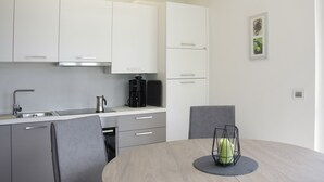 Una cocina moderna con armarios blancos, cafetera y una mesa de comedor con sillas.